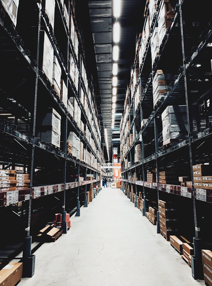 A wide aisle in a large warehouse filled with stacked boxes on high shelves.